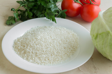 Raw rice in a plate and vegetables. Ingredients for cooking.