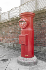 Old Japanese postbox stands beside a street in front of brick wall in a city of Japan (with Japanese language translated as Post)