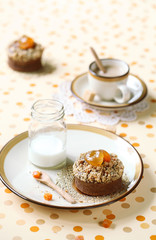 Chocolate Financier Cake with Apricots and Streusel Topping on plate, little bottle of milk and cup of coffee, on bright polka dotted background.