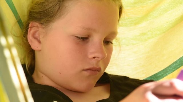 Teenager reads a book in her hammock in the summer sun