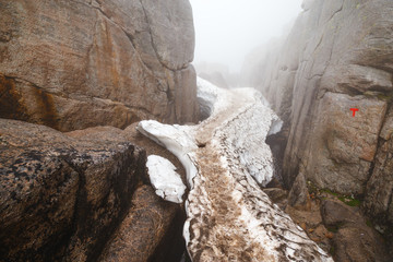Trekking snow trail throug canyon to Kjerag Kjeragbolten famous Norwegian natural landmark. Norway, Scandinavia, Europe. Beautiful misty scenery of northern nature.