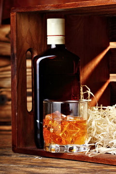 bottle and glass of whiskey with ice on a wooden background.