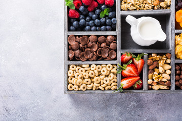 Variety of cold quick breakfast cereals with berries in old gray wooden box and other ingredients for breakfast, healthy eating concept, top view. Copy space.