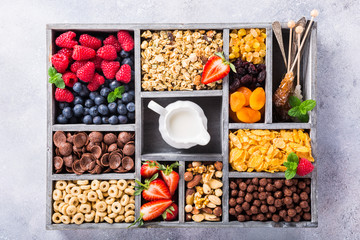 Variety of cold quick breakfast cereals with berries in old gray wooden box and other ingredients for breakfast, healthy eating concept, top view.
