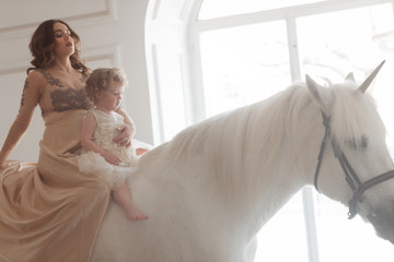 Lovely young pregnant woman and girl sits on horseback unicorn