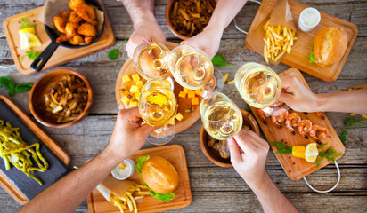 Hands with red wine toasting over served table with food.