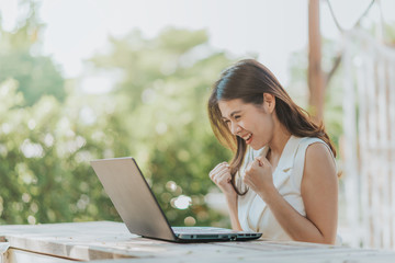 Happy successful Asian woman watching laptop on the desk outdoor