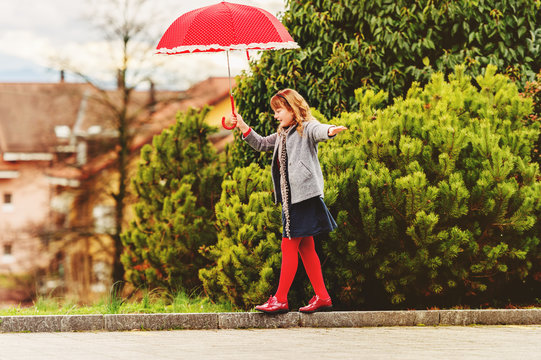 Funny little girl playing outdoors with big red polkadot umbrella