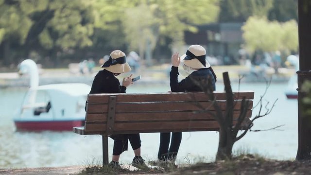 Women wearing hat sitting and chatting on park bench
