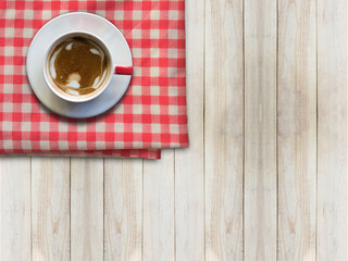 Hot coffee in white cup on red napkin on wooden table, top view