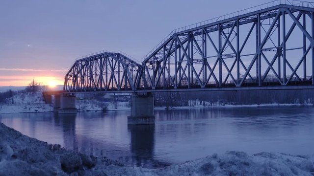 Time lapse of railway bridge over the river at dawn with a mountain forest and traffic highway in the background.