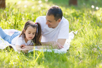 Young father and daughter lying on green grass. Happy daughter sitting on father back and smiling. looking up