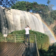 парень фотографирует на телефон водопад с радугой