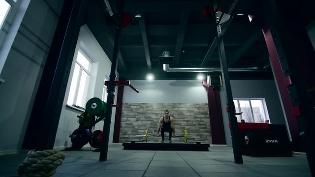 Medium shot slow mo tilt-down tilt-up men and women exercising and lifting weights female bodybuilder champion athlete doing power clean in cross fit gym