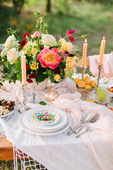 picnic, food, summer, holiday concept - close-up on part of the festively decorated table with a beautiful bouquet of roses and peonies, candles in candlesticks, apricots, cherries, pear, glassware