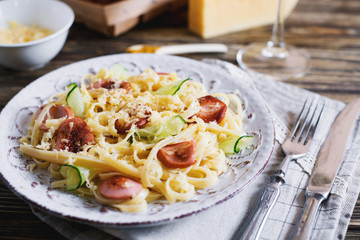 Italian food, vermicelli, spaghetti with fried sausages, cheese, cucumber, spices and white wine on a dark wooden background 