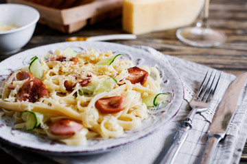Italian food, vermicelli, spaghetti with fried sausages, cheese, cucumber, spices and white wine on a dark wooden background 