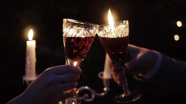 Closeup of crystal glasses with red wine in the hands of a couple during a romantic candlelit dinner