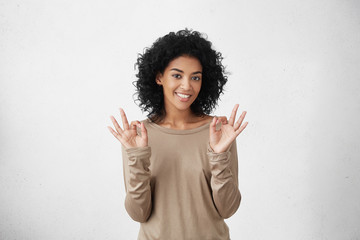 Everything is perfect. Happy positive dark-skinned student girl showing OK gesture with both hands,...