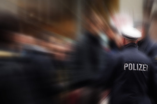 German police officer in action, shot from behind, focus on the jacket with POLIZEI lettering, that means police, blurred background with zoom effect, copy space