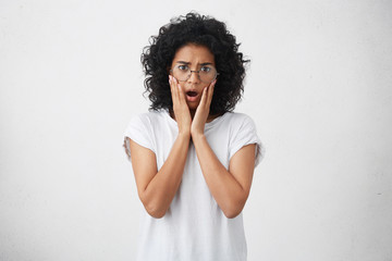 Pretty young black woman dressed in white T-shirt, wearing big round glasses, holding hands on...