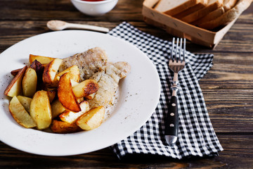 Delicious dinner, fast food, a national dish, fish with fried potatoes, fish and chips, sauce and white toast bread on a dark wooden background 