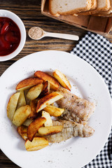 Delicious dinner, fast food, a national dish, fish with fried potatoes, fish and chips, sauce and white toast bread on a dark wooden background 