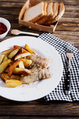 Delicious dinner, fast food, a national dish, fish with fried potatoes, fish and chips, sauce and white toast bread on a dark wooden background 