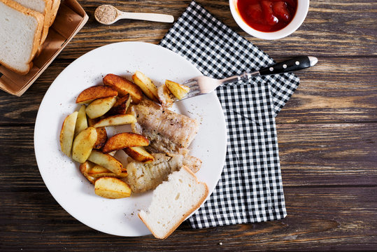 Delicious dinner, fast food, a national dish, fish with fried potatoes, fish and chips, sauce and white toast bread on a dark wooden background 