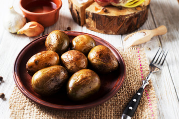 Russian and Ukrainian national cuisine, potatoes in their skin with fish, white bread, onions, garlic, cucumber and vegetable oil on a light wooden background 