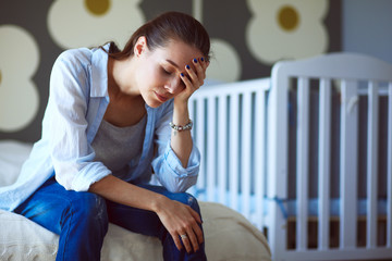 Young tired woman sitting on the bed near childrens cot