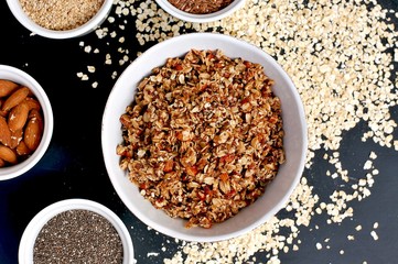 Homemade granola in white bowl with almond and seeds on black background