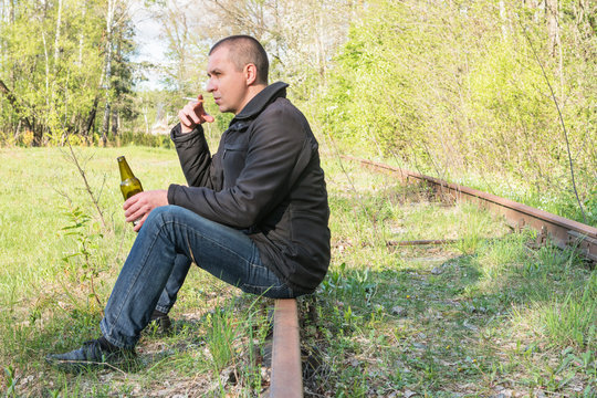Lonely man with a cigarette and a bottle of beer sitting on rusted rails