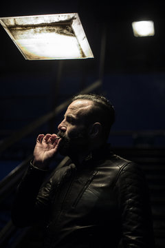 A middle aged, Egyptian man smokes in the streets of Brooklyn, New York City. He has a beard and is dressed in a leath jacket. Shot on a Spring night in 2017.