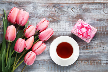 Pink tulips with gift box and cup of tea on wooden table
