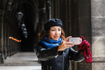 Woman tourist making selfie photo by smartphone on the background of an old gothic building