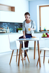 Young woman with orange juice and tablet in kitchen