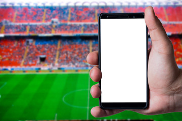 Mans hand holding a smartphone against soccer or football background.