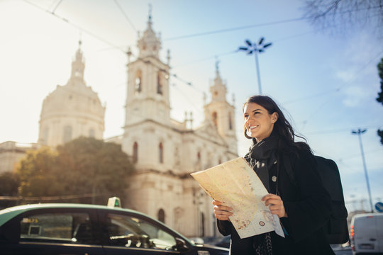 Admiring amazig sunset in european metropola.Traveling in Europe.Female turist in front of Basilica da Estrella and famous 28 tram in Lisbon,Portugal.Woman holding maps and exploring charming country