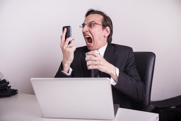 Angry and frustraded business man screaming on a cell phone in the office
