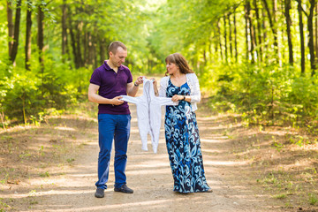 Portrait of a caucasian pregnant woman and her husband hold clothes for baby outdoors