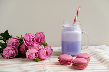 Purple coffee in stylized mason jar cup with macarons and roses and colorful decoration. Blueberry milk shake. Unicorn coffee. Unicorn food