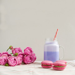 Purple coffee in stylized mason jar cup with macarons and roses and colorful decoration. Blueberry milk shake. Unicorn coffee. Unicorn food