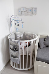 newborn lies in the round white bed with mobile and toys
