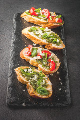 Italian food. Snacks. Antipasto. Bruschetta with pesto sauce, parmesan cheese, tomatoes and fresh basil. On black table, on slate board. With glass of red wine. Top view copy space selective focus