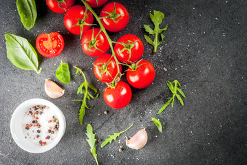 Cooking, background. Ingredients for cooking. Spices (salt pepper) greens (Arugula parsley basil) and cocktail cherry tomatoes on a black stone table. Top view copy space