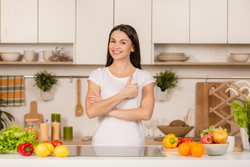 Young cooking woman standing near desk smiling, looking at camera, shows thumbs up