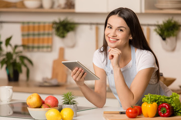 Young Woman standing in kitchen with tablet computer and looking recipes.