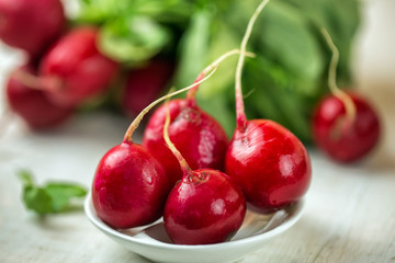 Red radishes in bowl on wooden table. Vegetable of cabbage family. 