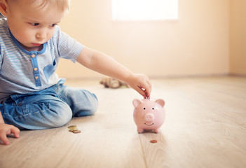 two years old child sitting on the floor and putting a coin into a piggybank